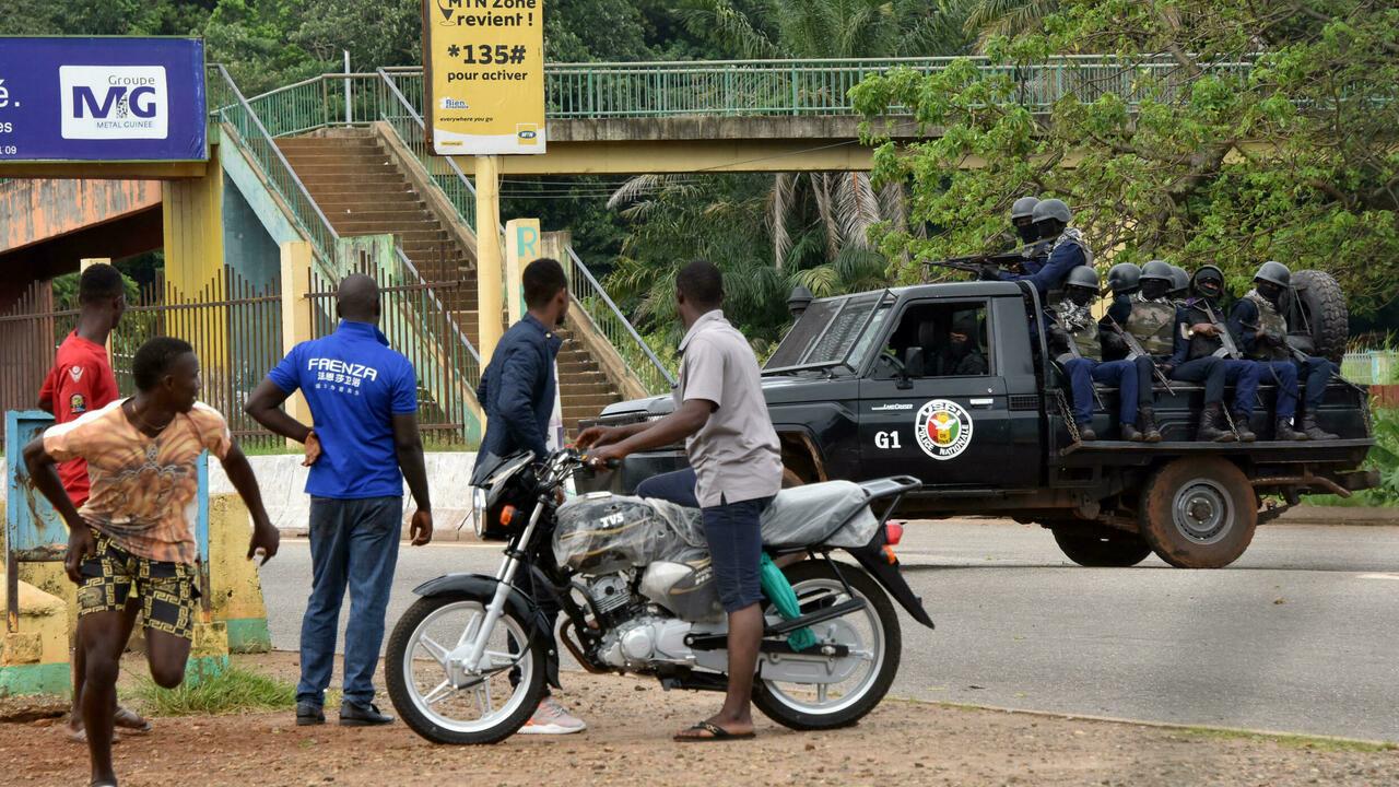People look on as members of the Guinean Police National drive through the central neighbourhood of Kaloum in Conakry on September 5, 2021 after sustainable gunfire was heard. – Gunfire was heard in Conkary in the morning and troops were seen on the streets, witnesses told AFP. There was no immediate explanation for the incidents in Conakry’s Kaloum peninsula, where the presidency, various institutions and offices are located. (Photo by CELLOU BINANI / AFP)